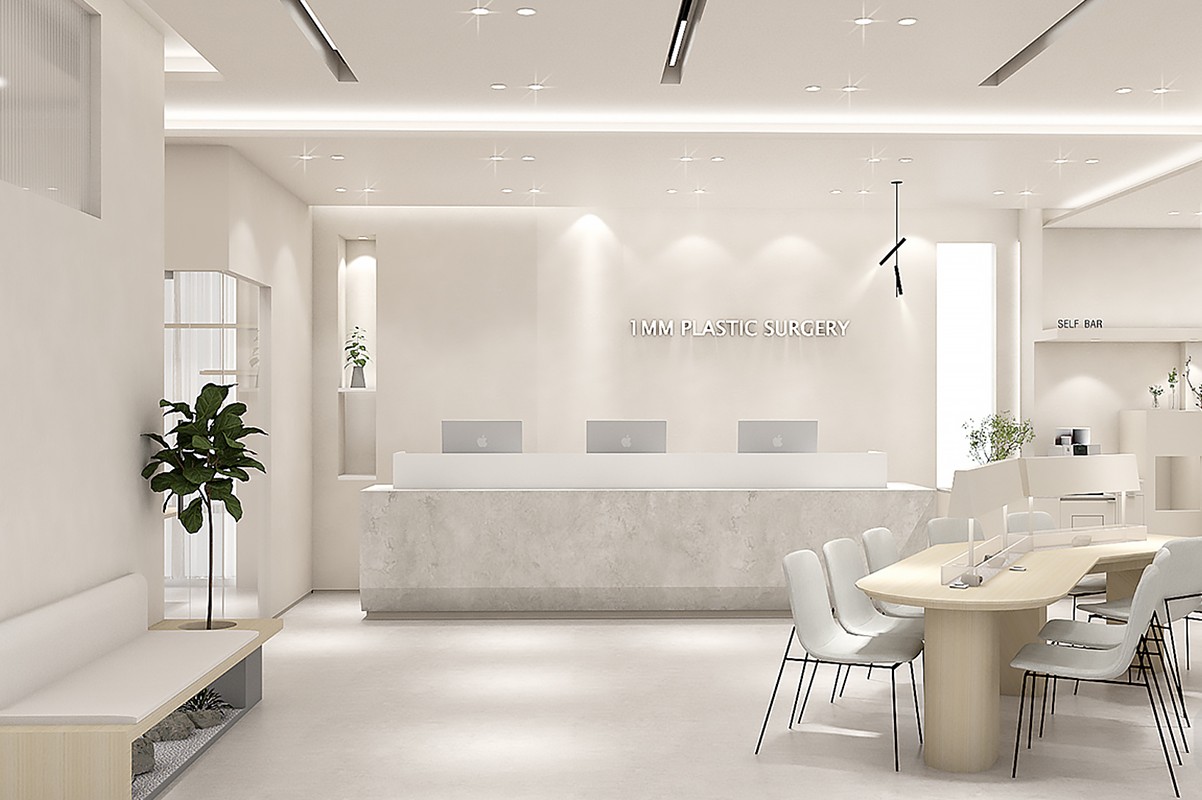 An interior image showing a white marble reception desk, a wall behind it with '1MM PLASTIC SURGERY' lettering, and a long oval wooden table with partitions and white chairs at the front right.